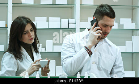 Female and male pharmacists working in pharmacy, talking via smart phone and checking pills Stock Photo