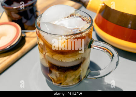 a glass mug of iced coffee with milk forming the storming patterns of Jupiter and Saturn on the table with old fashioned 70s kitchenware Stock Photo