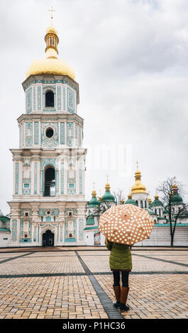 Young woman stands under umbrella in square and in front of Bell tower of St. Sophia Cathedral, Kiev, Ukraine Stock Photo