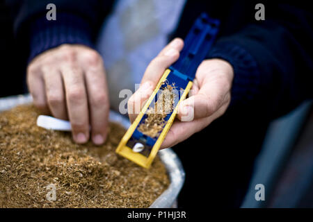 Close-up of a street tobacco vendor in Istanbul, Turkey rolling a cigarette with a hand held machine. Very shallow depth of field, focus on machine. Stock Photo