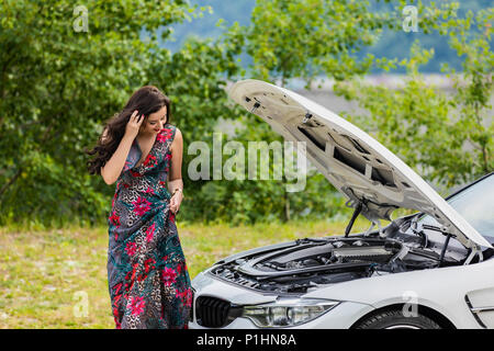 Young woman waits for assistance near her car broken down on the road side. Stock Photo