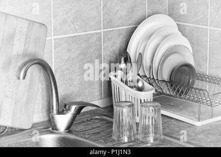 Washed plates, cutlery and glasses, drying in their racks close to the sink in the kitchen Stock Photo