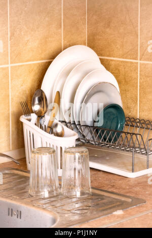 Washed plates, cutlery and glasses, drying in their racks close to the sink in the kitchen Stock Photo