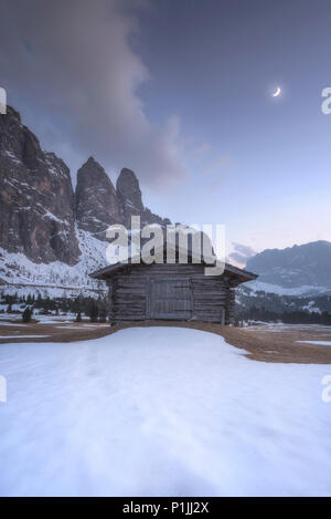 Wooden hut and melting snow with first quarter moon at Grödner Joch (Passo Gardena) in the Dolomites, Trentino-South Tyrol, Italia, Europe Stock Photo