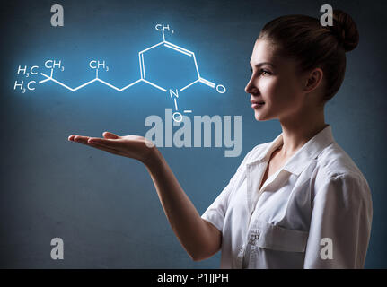 Young female doctor presents chemical formula. Over dark background. Stock Photo