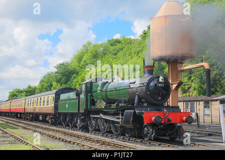 Landscape shot: puffing steam engine Bradley Manor (7802) & rake of carriages, waiting on track under water tower, southern end of SVR Bewdley station. Stock Photo