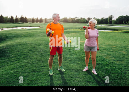 senior man and woman practice fitness exercise with dumbbells in a park at sunny day Stock Photo