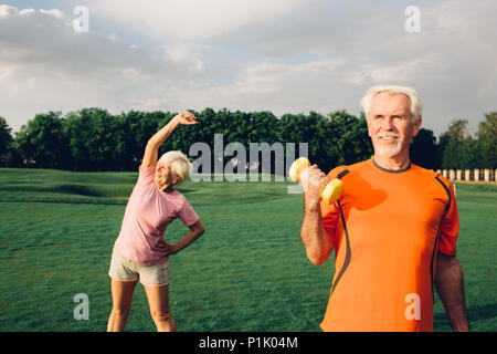 senior man and woman working out with dumbbells in a park at sunny day, focus on man Stock Photo