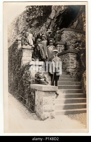 THE CZECHOSLOVAK REPUBLIC - CIRCA 1940s: Vintage photo shows people stand on the stairs outdoors. Some of them wears leather helmet for driving of car. Black & white antique photography. Stock Photo