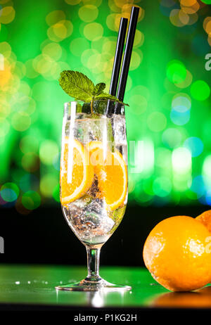 Fresh cocktail with orange, ice and mint leaves. Alcoholic, non-alcoholic drink-beverage at the bar counter in the night club. Colorful bokeh on a gre Stock Photo
