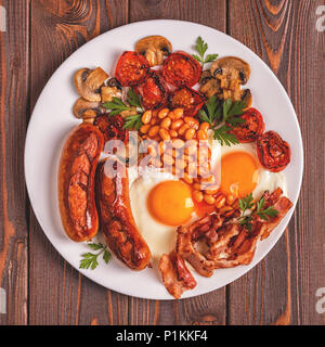 Traditional full English breakfast with fried eggs, sausages, beans, mushrooms, grilled tomatoes and bacon on wooden background. Top view Stock Photo