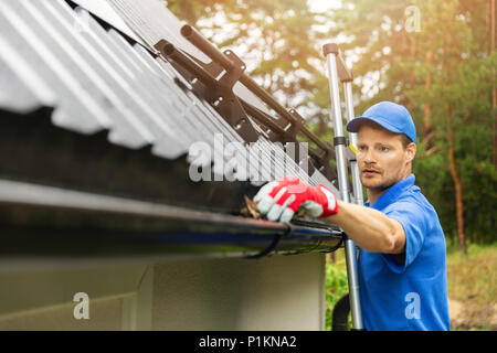 worker cleaning house gutter from leaves and dirt Stock Photo