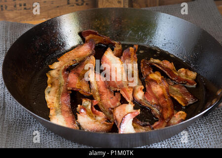 Cooked streaky bacon in a cast iron skillet Stock Photo