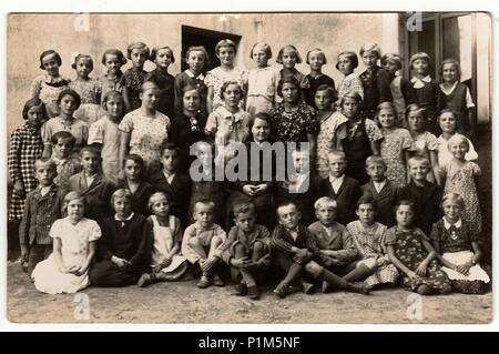 THE CZECHOSLOVAK REPUBLIC - SEPTEMBER 30, 1936: Vintage photo shows pupils (schoolmates) and their schoolmistress pose in front of school. Black & white antique photography. Stock Photo