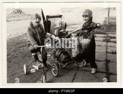 THE CZECHOSLOVAK SOCIALIST REPUBLIC - CIRCA 1970s: Retro photo shows children who play with pram and tricycle.  Black & white vintage photography. Stock Photo
