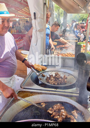 Hispanic cook frying Entresijos (Lamb Mesentery) in a stall of a Street Food fair. Others cookers cooking Sausages and Oreja de Cerdo (Pork Ear) Stock Photo