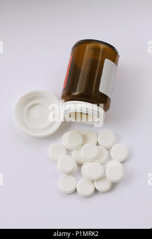 White pills spilled from fallen pill bottle. Top view of pills and medicine container lying on white background illustrating drug addiction. Close up  Stock Photo