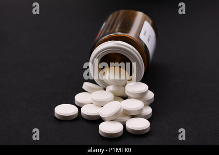 White pills spilled from fallen pill bottle. Pills and medicine container lying on black background illustrating drug addiction. Close up stock image Stock Photo