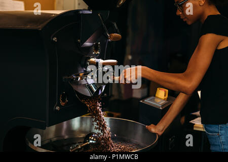 Young barista opening a coffee roaster, beans falling out into the cooling pan Stock Photo
