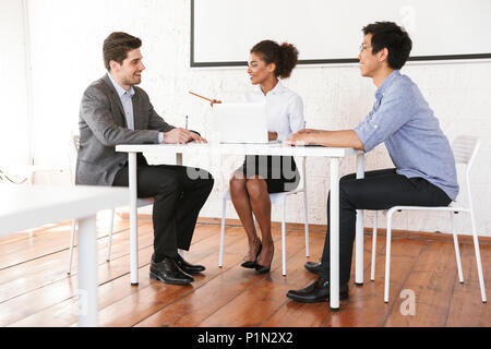 Group of smiling young multiethnic businesspeople sitting at the desk and talking Stock Photo