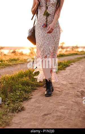 Cropped photo of stylish caucasian woman wearing dress walking on road in countryside during sunny summer day Stock Photo