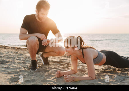 Happy young sport couple doing plank exercise at the beach Stock Photo