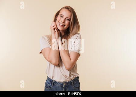 Image of positive blonde woman 20s wearing casual clothing smiling and looking at camera pressing arms at chest isolated over beige background in stud Stock Photo