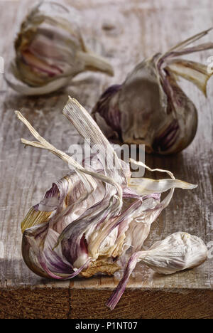 Garlic bulb remains after use of garlic cloves on rough whitewashed wooden plank. Still life close up with selective focus. Stock Photo