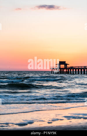 Naples, Florida pink and orange sunset vertical view in gulf of Mexico with sun setting inside Pier wooden jetty, horizon and dark blue ocean waves Stock Photo
