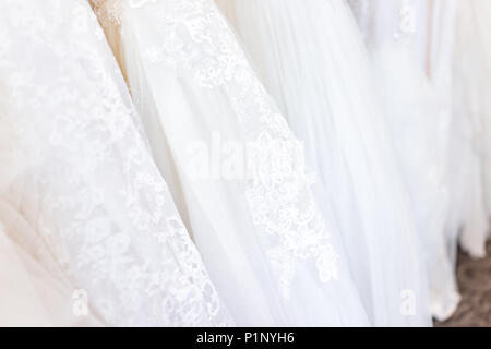 Many wedding dresses on rack in boutique discount store, white garments hanging hangers row closeup with white lace, tulle, design Stock Photo