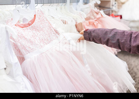 Young woman touching one wedding flower girl party dress in boutique discount store, pink garments hanging on rack hangers row closeup with white lace Stock Photo