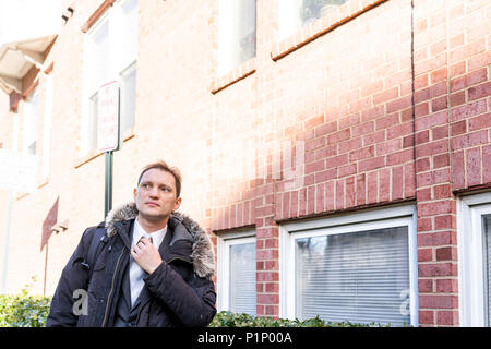 Young serious businessman face standing in front of brick wall, fixing tie, in suit and tie on interview break outside Stock Photo