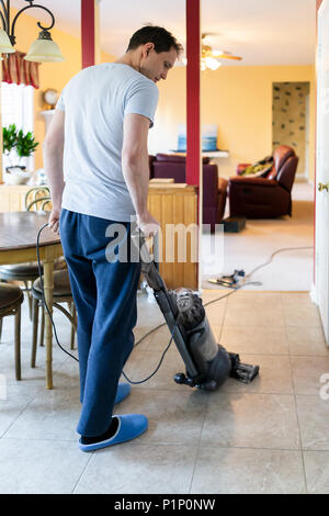 Young man house husband vacuuming using vacuum on tile floor inside interior of house kitchen room by table, domestic life Stock Photo