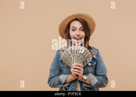 Portrait of a smiling young girl in summer clothes showing money banknotes and looking at camera isolated over beige background Stock Photo