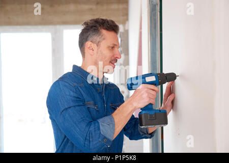 Handyman using cordless drill while working on construction site. Stock Photo