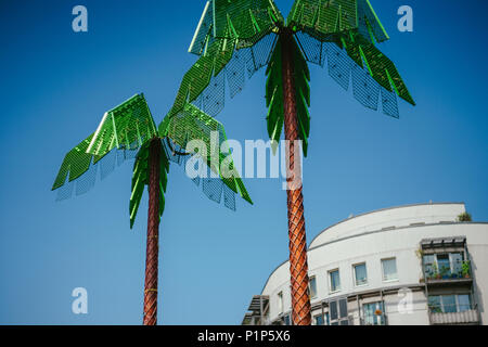 Artificial green metal palms with white living house and blue sky background in Park Fiction Hamburg. An artistic and sociopolitical project located in small park near St. Pauli, Hamburg Stock Photo