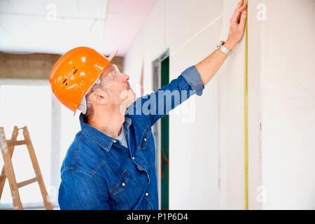 The handyman using a tape measure while working on construction site. Repairman wearing safety hardhat and protective eye goggles. Stock Photo