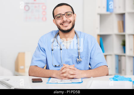 Cheerful Middle-Eastern Doctor Posing at Desk Stock Photo