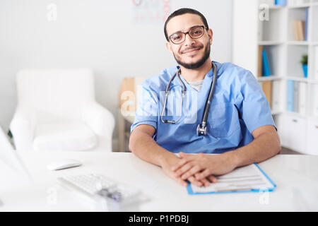 Middle-Eastern Doctor Posing at Desk and Smiling Stock Photo