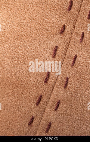 neat row of large running stitches in a brown tan suede fabric at a slanting angle Stock Photo