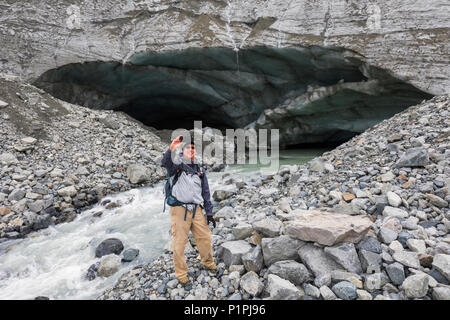 Male hiker takes a self-portrait with his cell phone in front of a Gulkana Glacier ice cave;Alaska, United States of America Stock Photo