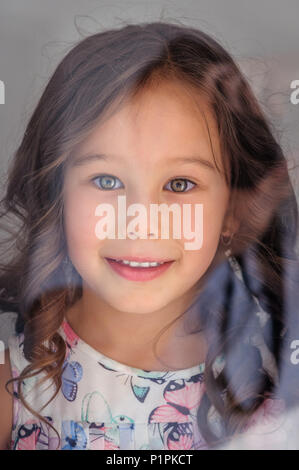 Portrait of a cute caucasian five years old girl smiling behind a window glass Stock Photo