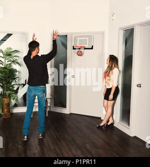 Two young millennial business co-workers taking a break in the workplace and shooting a basketball into a net; Sherwood Park, Alberta, Canada Stock Photo