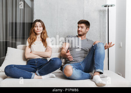 Confused young couple having an argument while sitting together on a couch at home Stock Photo