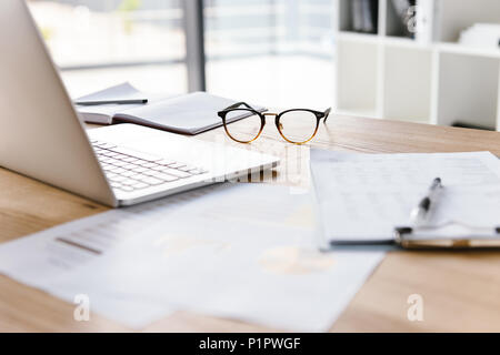 Image of workplace in office room without people with open laptop, clipboard, glasses pencil and notebook lying on wooden desk Stock Photo