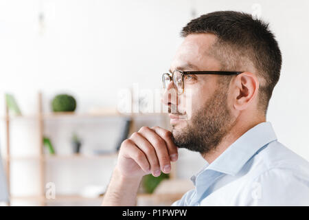 Profile portrait closeup of handsome concentrated man 30s wearing white shirt and glasses looking ahead while working in office room at business centr Stock Photo