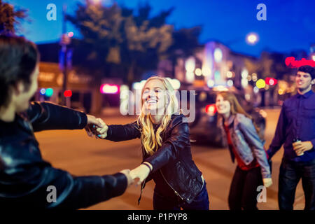 Two young couples being playful on the sidewalk beside a city street at dusk; Edmonton, Alberta, Canada Stock Photo