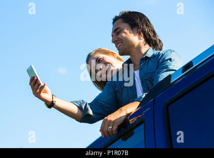 A young couple stand up through the sunroof of their vehicle and take a self-portrait with their cell phone; Edmonton, Alberta, Canada Stock Photo