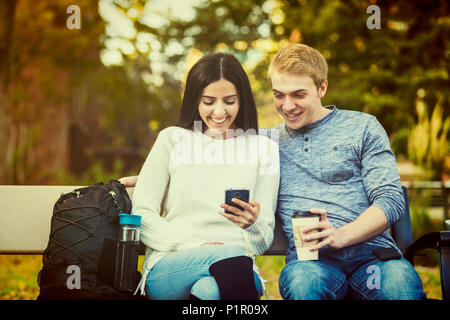 Young dating couple who are university students sitting on a bench on campus and looking at social media on a smart phone; Edmonton, Alberta, Canada Stock Photo