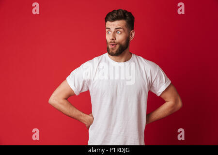 Picture of excited young handsome man standing isolated over red wall background. Looking aside. Stock Photo